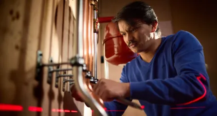 Profielfoto bij de functie van een monteur warmte in de sector energie. Man bevestigt koperen leidingen met behulp van een waterpas-laser in een technische werkplek.