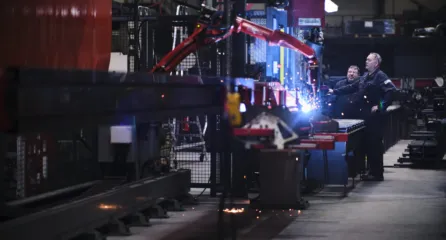 Profielfoto van twee medewerkers werken met een lasrobot in een fabriekshal waar vonken overspringen.