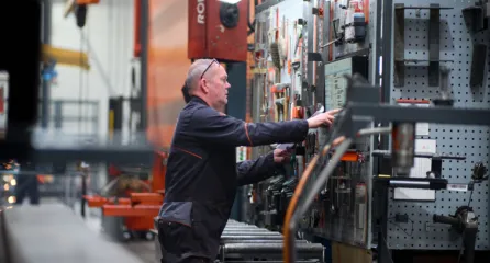 Profielfoto bij functie technisch medewerker. Man bedient een machine en controleert instellingen in een werkplaats.