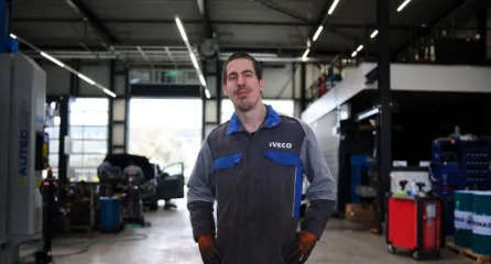 Profielfoto bij de functie autoruitschadehersteller in de sector mobiliteit. Man staat in beschermend pak midden in een werkplaats en kijkt in de camera.