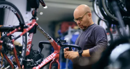 Profielfoto bij de functie assistent fietsenmaker in de sector mobiliteit. Man is aan het werken aan een fietsstuur in een werkplaats.