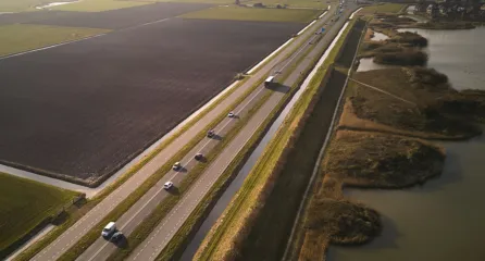 Profielfoto van snelweg met auto's en weilanden en water.