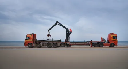 Profielfoto bij vrachtwagens met hijskraan laden of lossen materialen op het strand.