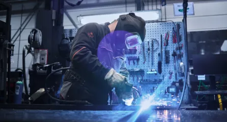 Profielfoto van de functie lasser met beschermkap last metalen onderdelen, terwijl vonken en blauw licht zichtbaar zijn.