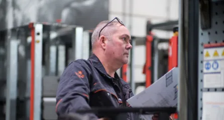 Profielfoto van technisch medewerker bekijkt computer in een werkplaats met metalen constructies.