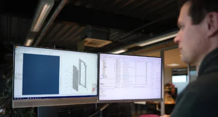 Profielfoto van technisch ontwerper bekijkt een 3D-model en technische tekening op twee computerschermen.