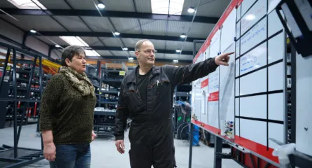 Profielfoto van twee medewerkers bespreken de planning bij een groot whiteboard in een werkplaats.