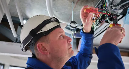 Profielfoto bij de functie monteur gas in de sector energie. Draagt PBM's en werkt aan elektrische bedrading in een plafondinstallatie.