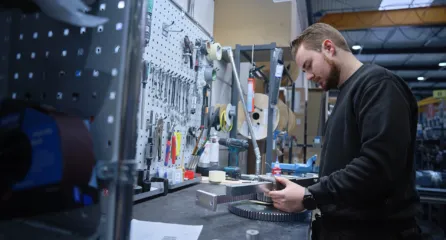 Profielfoto bij de functie medewerker assemblage. Een monteur werkt aan een metalen onderdeel aan een werkbank vol gereedschap.