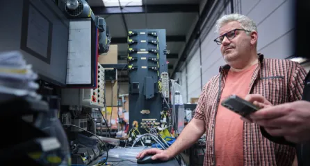 Profielfoto van een technicus die een testopstelling bedient met bedrading en meetapparatuur in een werkplaats.