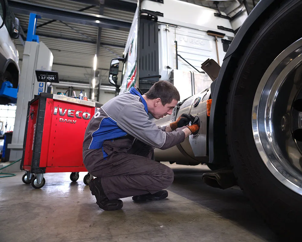 Profielfoto bij de functie carrosseriebouwer in de sector mobiliteit. Man hurkt en sleutelt aan een auto met gereedschap.