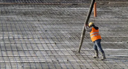 Profielfoto van functie betonwerker. Twee mannen die beton storten met een grote slang op een gele vloer.