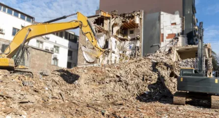 Profielfoto van functie sloper. Een gele en donker grijse graafmachine die een gebouw aan het slopen zijn
