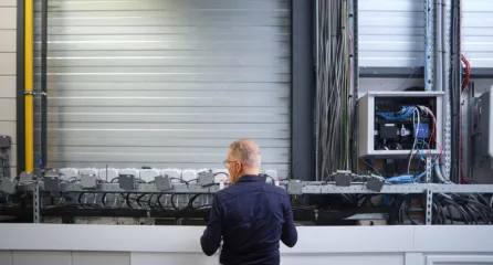 Profielfoto bij de functie kwalitet en veiligheid in de sector energie. Een man bekijkt een technische installatie met kabels en apparaten in een industriële omgeving.