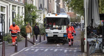 Profielfoto van functie belader. Twee mannen in veiligheidskkeding beladen een oranje vuilniswagen