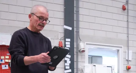 Profielfoto van functie werkvoorbereider. Man met donkerblauwe trui en bril kijkt op een Ipad die hij in zijn handen heeft.