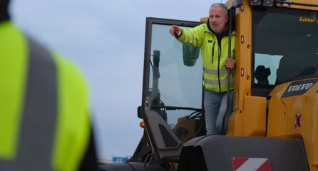 Profielfoto van uitvoerder. Man in gele veiligheidsjas geeft aanwijzingen vanuit de cabine van een shovel.