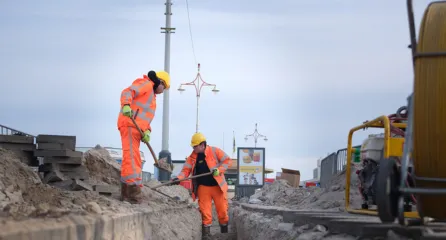 Profielfoto bij functie vakman grond water weg in de sector infa. Twee vakmannen in veiligheidshesjes leggen kabels of leidingen aan in zandige bouwput langs de weg.