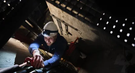 Profielfoto bij de functie eerste monteur service en onderhoud in de sector installatietechniek. Een monteur met veiligheidshelm werkt met gereedschap in een smalle ruimte.