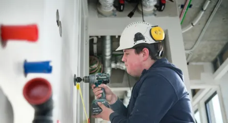 Profielfoto bij de functie hulpmonteur in de sector installatietechniek. Jongeman boort in een muur binnen een gebouw.