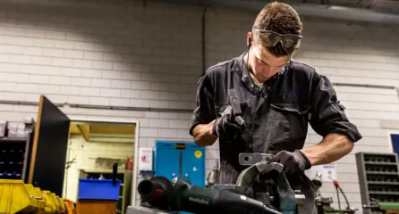 Profielfoto van de constructiebankmedewerker. De constructiebankmedewerker werkt met een hamer om een stuk metaal te bewerken