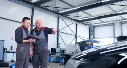 Profielfoto bij de functie schademanager in de sector mobiliteit. De service adviseur wijst naar een auto om iets aan te wijzen voor monteur die naast hem staat.