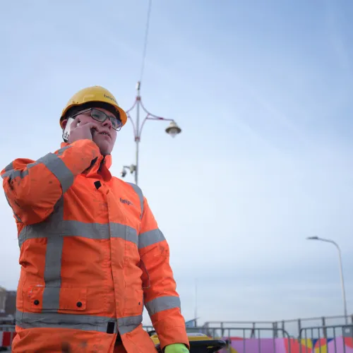 Een foto van een uitvoerder in de bouw in PBM's die aan de telefoon is.